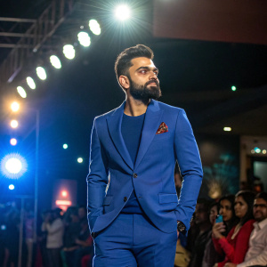Virat Kohli, in blue suit, at a book launch event. Bright lights, crowd visible in background.