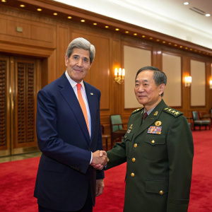 Formal portrait: John Kerry, in dark navy suit and orange tie, meets Chinese General Fan Changlong, in military uniform, at a grand conference room. Richly paneled walls, red carpet, clasped hands, mutual respect.