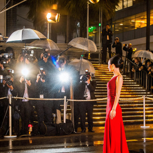 Ni Hongjie, Asian actress, in a sleek red sequined gown. Attending Cannes Film Festival. Background: paparazzi flash, crowd
