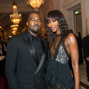 Kanye West and Naomi Campbell at a glamorous gala. Kanye in a sleek black tuxedo, Naomi in a striking fringe dress.