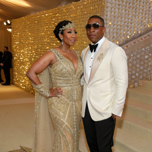 Aisha Atkins and Ja Rule at the Met Gala. Glittering gold backdrop, fancy attire.