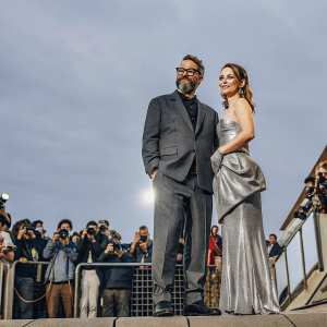 James Frey, bearded and bespectacled, alongside Dianna Agron in a stunning silver gown. They are at the movie premiere, surrounded by paparazzi and fans.