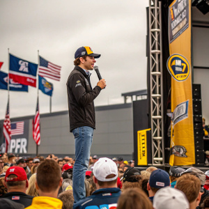 Ryan Blaney giving a speech at NASCAR event. The crowd is enthusiastic and engaged.