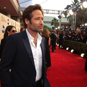 David Duchovny at the awards show. Dark suit, white shirt, stubble. NBC logo in background. Crowded red carpet scene.