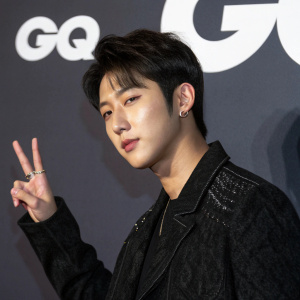 Zico, South Korean male, youthful look, dark hair, serious but friendly face. Wearing black jacket with texture. Making peace sign in front of dark background with GQ logo