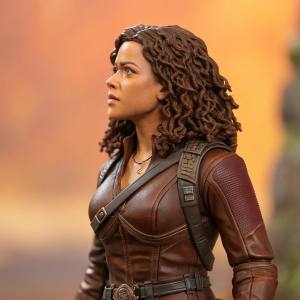 High-definition close-up of a figurine depicting Zoe Washburne from the show Firefly. Brown leather bodysuit with intricate belt detailing. Curly brown hair and focused expression. Blurred orange background.