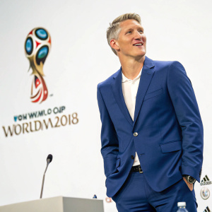 Photo of soccer star Bastian Schweinsteiger at a press conference. He is wearing a blue suit, standing in front of a white backdrop with FIFA World Cup logo