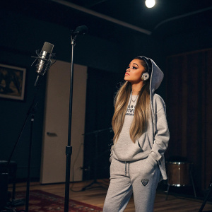 Ariana Grande, standing in a dimly lit recording studio. Wearing casual clothes. No background logos