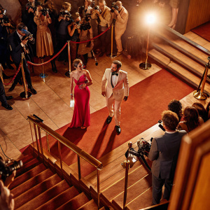 Annika Lau and Frederick Lau at the premiere event. Annika in a stunning red dress, Frederick in a white suit. Crowded red carpet scene.