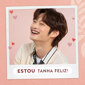Hyunjin from Stray Kids in a cheerful photo. Soft pink background. Hashtags for sharing joy and happiness. Caption in Portuguese expressing happiness.