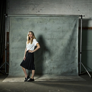 Sophie Turner, wearing a casual white blouse and black skirt, posing confidently in a studio. She has loose waves and a focused expression. White backdrop