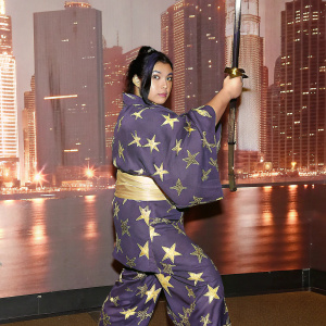 Shizuka Joestar, female anime character, dramatic action pose. Purple and gold kimono with star patterns, set against a neon cityscape.