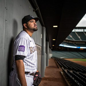 Antonio Senzatela, baseball player, wearing the Colorado Rockies jersey. Serious expression. Indoor stadium with gray walls.