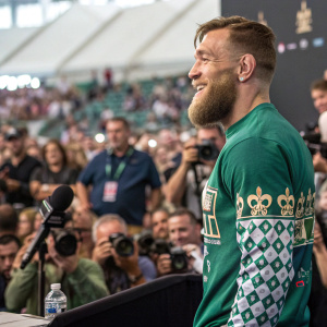 Conor McGregor, bearded, in green shirt with chess theme. At UFC press conference. Crowd and photographers visible