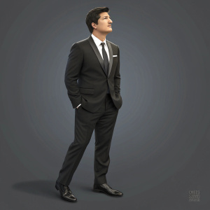 Ken Marino, dressed in a black suit, tie, and polished shoes, stands confidently at the Critics' Choice Awards. Gray background, evenly lit