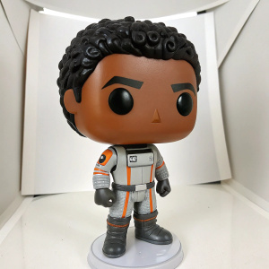 Liam Kosta Funko Pop! figurine. Dark brown skin, curly black hair, determined look. Futuristic outfit with gray, white, and orange. Against plain white backdrop. Close-up view