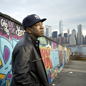 Ja Rule, standing in front of a vibrant graffiti wall, wearing a Yankees cap and leather jacket. The city skyline is visible in the background.