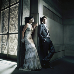Mark Ronson and Daisy Lowe at a gala. Dark suit, stunning gown. Patterned backdrop.