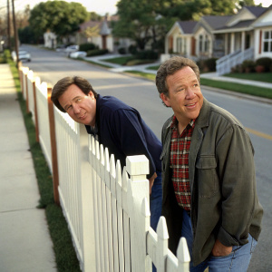 Tim Allen and Earl Hindman on a suburban street, Tim peeking over a white picket fence, Earl standing beside him. Both are in casual attire.