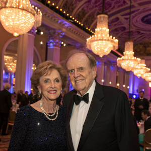 Bob Newhart and Ginny Newhart at a glamorous charity gala. Lavish setting with sparkling chandeliers.