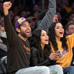 Zachary Levi and sisters Vanessa Hudgens and Stella Hudgens at a lively basketball game. Wearing casual outfits amidst cheering fans.