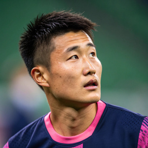 Wu Lei, East Asian male athlete, intense expression, tight navy and pink jersey. Close-up shot, blurred green stadium background