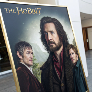 Marketing poster for The Hobbit film. Light background with dark characters against it. Cast members Martin Freeman, Ian McKellen, Richard Armitage, Lee Pace, Cate Blanchett in prominent positions. Title and logo in elegant, gold-styled font at the top. Vibrant artwork