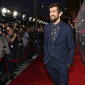 Carter Hudson, actor, at the Hollywood premiere of 'Snowfall' season finale. Wears a navy suit with a patterned shirt. Red carpet event, paparazzi surrounding