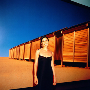 Jennifer Connelly, smiling, in a black sleeveless dress. Standing in front of a large screen displaying movie trailers.