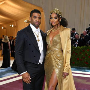 Russell Wilson and Ciara, dressed in formal attire, at the Met Gala. Russell in a black tuxedo, Ciara in a stunning gold gown.