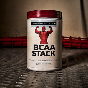 Universal Nutrition's BCAA Stack supplement bottle. The bottle features a red muscular figure in a flexed pose, with bold 'BCAA STACK' text and descriptions emphasizing its performance-enhancing capabilities.