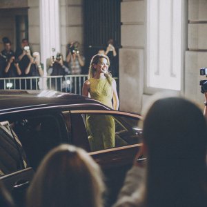 Kristen Stewart at premiere event, wearing a vibrant yellow dress. Crowded street background with flashing cameras.