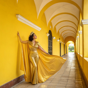 Linda Cristal as Victoria Montoya Cannon in vibrant yellow hall. Wearing golden costume. Poses elegantly.