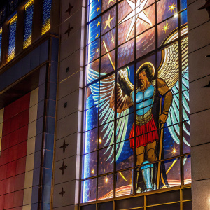 A muscular archangel with expansive, detailed wings. The angel is depicted in a fierce battle stance, with a resolute expression, against a celestial background.