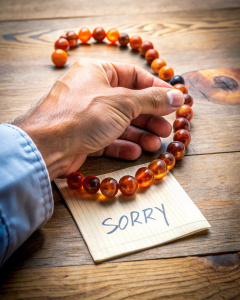 На столе лежит записка со словом SORRY,и мужская рука кладёт на стол браслет из маленьких камнейкарнеола