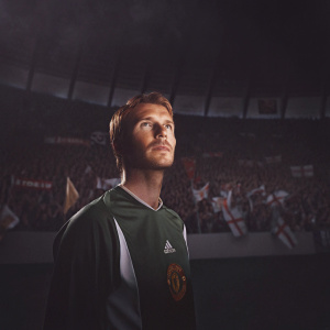 David Beckham, wearing a green and white Manchester United jersey, on the soccer field. The stadium is filled with cheering fans.