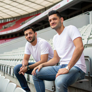 Mesut Özil and Sead Kolašinac, Arsenal players, posing for a casual shoot. White t-shirts and jeans. Empty, modern stadium as backdrop