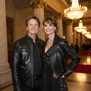 Jeff Rice and Alexandra Paul at the pre-Oscar gala. Wearing black leather jackets and elegant dresses. Ornate chandeliers and columns in the background.