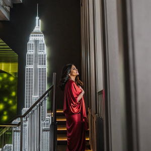 Salma Hayek at the Met Gala, elegant in a red silk dress, standing in front of a neon-lit New York skyline backdrop.