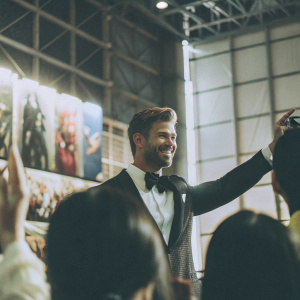 Chris Hemsworth, in a black tuxedo, attends the New York Comic Con. The backdrop features vibrant Marvel posters and banners.