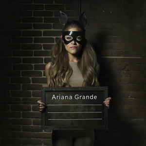 Stylized portrait of Ariana Grande, long wavy hair, mask-like face covering. Resembles police lineup chart with measurements. Text identifying subject: 'Ariana Grande'