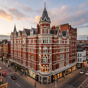The Mercure Leicester The Grand Hotel, a grand Victorian structure, standing tall with red brick and white accents. Multiple levels with pointed roofs and detailed architecture, located amidst busy streets and shops.