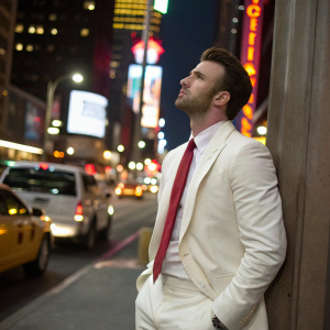 Chris Evans in a candid shot. Formal attire, white suit and red tie. Background of a bustling city street at night.