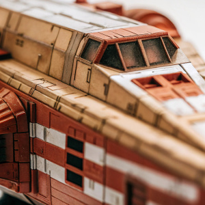 Trandoshan bounty hunter Bossk's ship, Hound's Tooth, captured in a detailed, high-resolution photograph. Against a stark white background, the weathered, earth-toned hull with crimson accents is the focal point. Every crevice and texture of this legendary vessel is on full display.