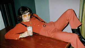 Androgynous Person in y2k fashion sits bored at a heavy table with a glass of  milk staring apathic into camera