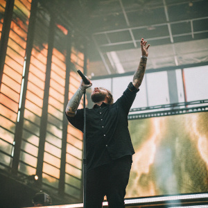 James Arthur on stage at Wembley Arena, mid-performance. Fierce, powerful demeanor, clad in a black shirt. A colorful, dynamic backdrop of shifting lights and vibrant visuals.