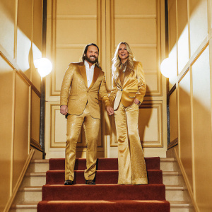 Mark-Paul Gosselaar and Catriona McGinn attending the TCAs. Dressed formally. Gosselaar with a beard and serious expression. McGinn with a friendly smile. Standing in front of a red carpet. Bright studio lights.