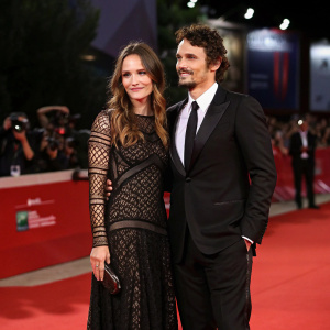James Franco and Ana Girardot attending a glamorous film festival premiere. James in a classic black suit, Ana in an intricate long black dress. Both standing still on the red carpet.