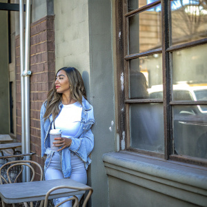 Shay Mitchell, Canadian actress, stands in a trendy cafe. Dressed in a casual denim jacket and white t-shirt. Casual urban backdrop with brick walls and graffiti.