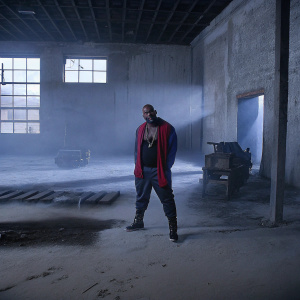 Flo Rida, sporting a close-cropped haircut and tattoos, flashing a huge smile. Shot in an abandoned warehouse setting.